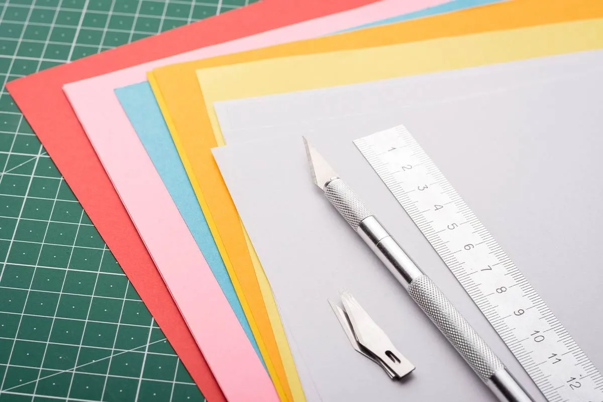 Pile of coloured paper fanned out with a ruler on top to make origami sheep.