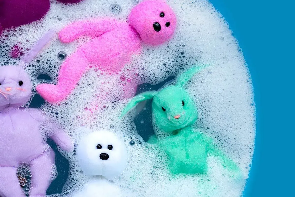 Colourful soft toy bears soaking in a tub of soapy water.