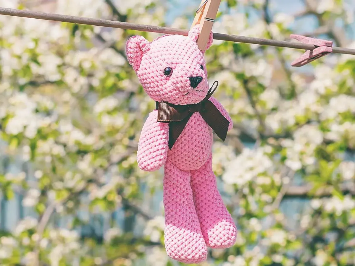Pink teddy bear air drying on the washing line after being washed.
