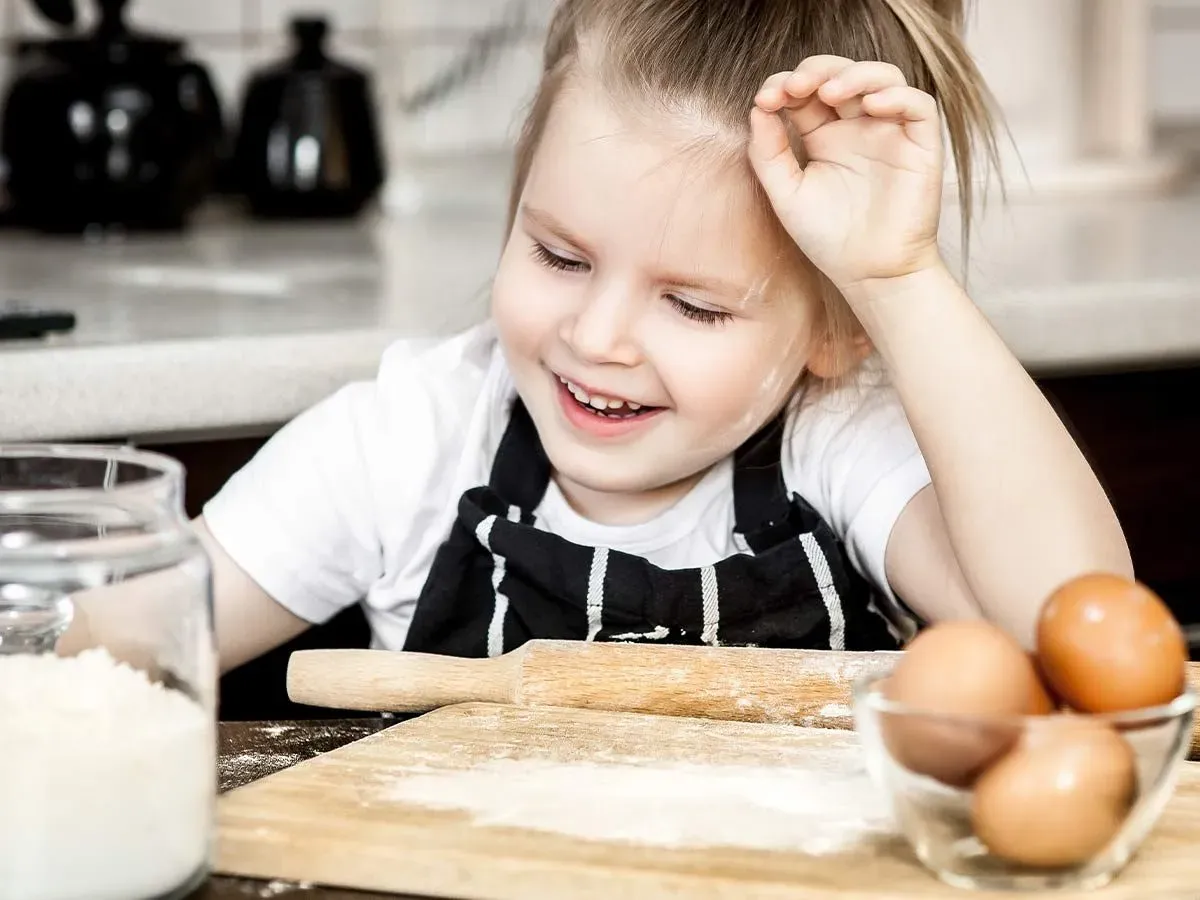 Little girl in the kitchen with flour on her face as she helps her mum make a monkey cake.