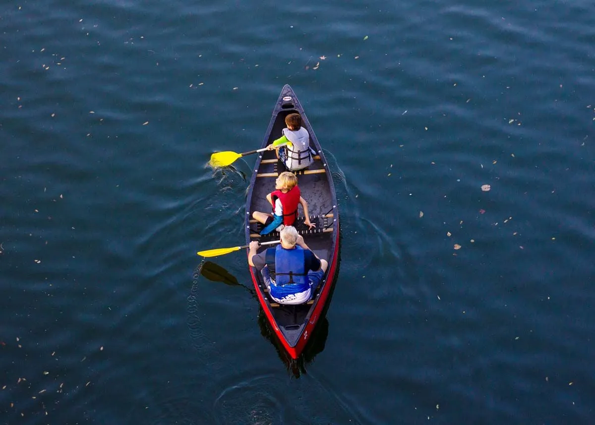 Three boys wearing life vests as they row on the water in a canoe.