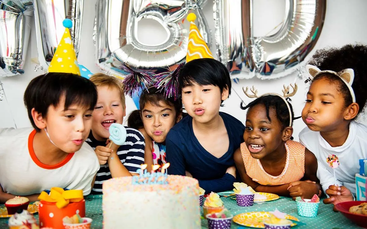 Kids blowing out the candles at a birthday party with friends at home.