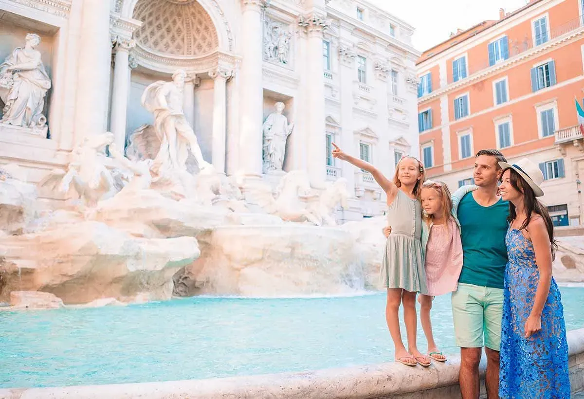 Happy family on holiday in Rome standing by the Trevi Fountain, little girl pointing to Roman architecture she learned about in school.