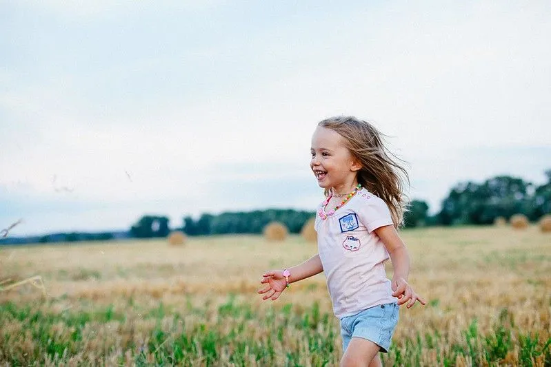 A little girl laughs as she runs through a field of crops.
