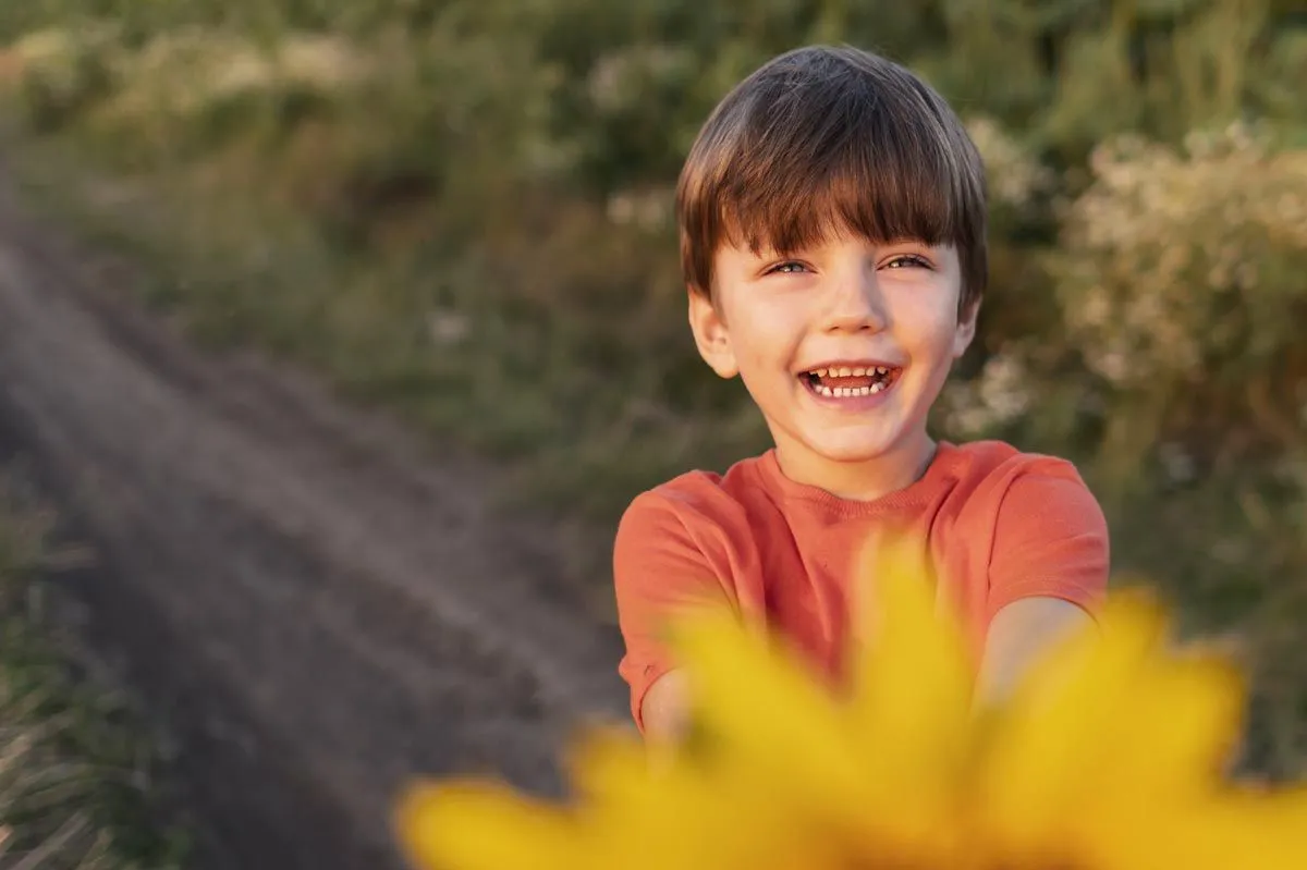 A young boy holding a flower laughs into the camera.