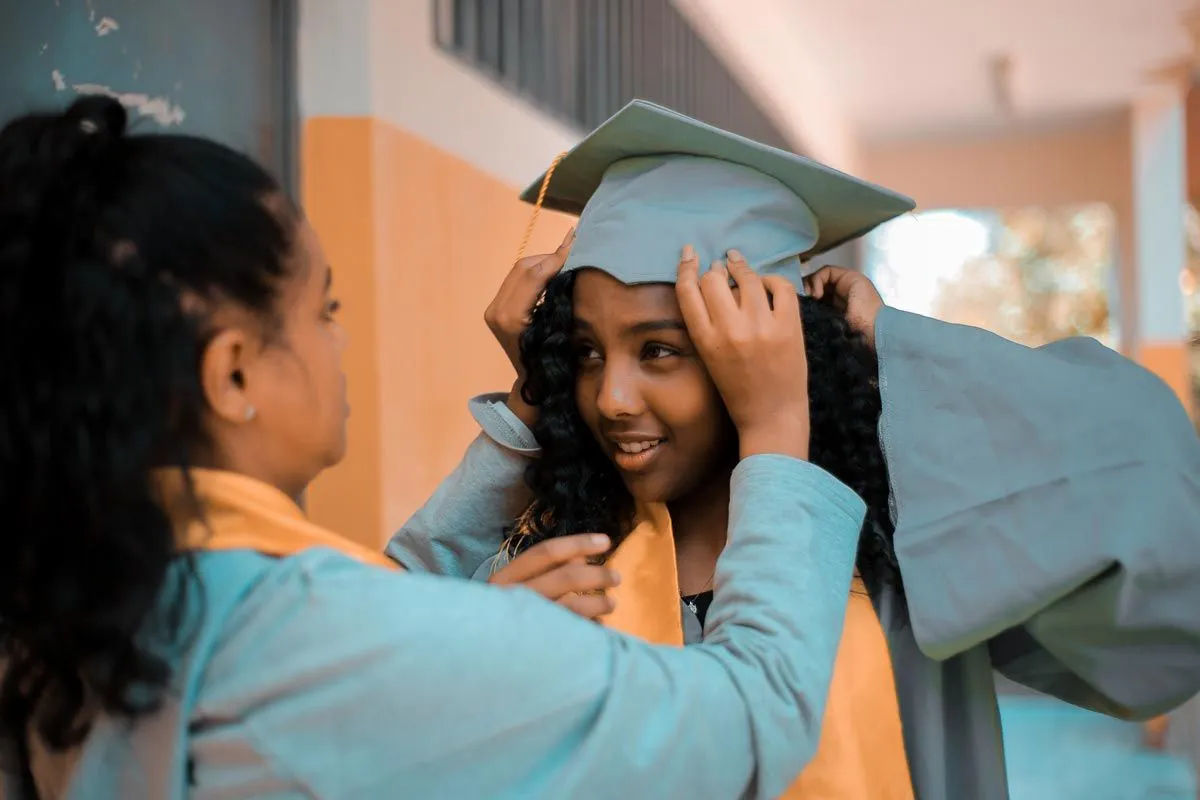 A young girl adjusts her friend's graduation cap.