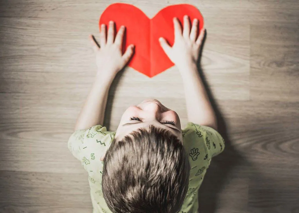 An image from above of a little boy holding a red heart cut out of cardboard.