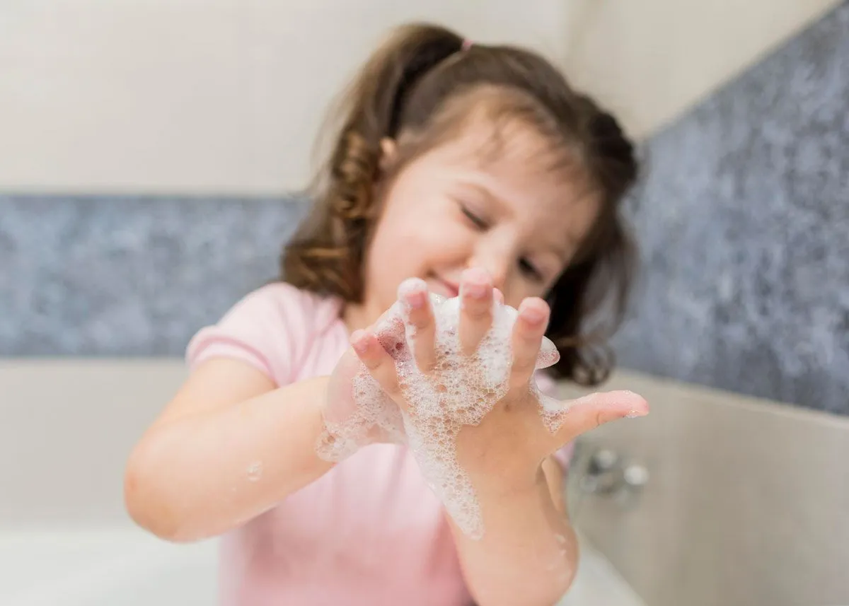 Little girl playing with soapy bubbles on her hand as she sits in the bath tub.