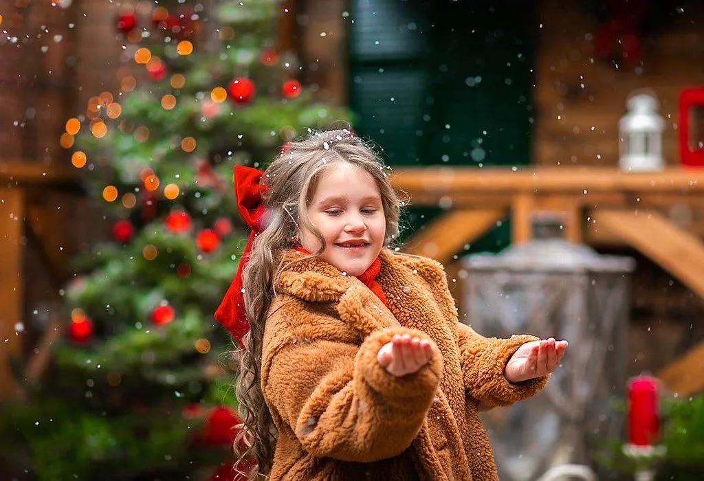 A little girl puts her hands out to catch falling snow at Christmas time.