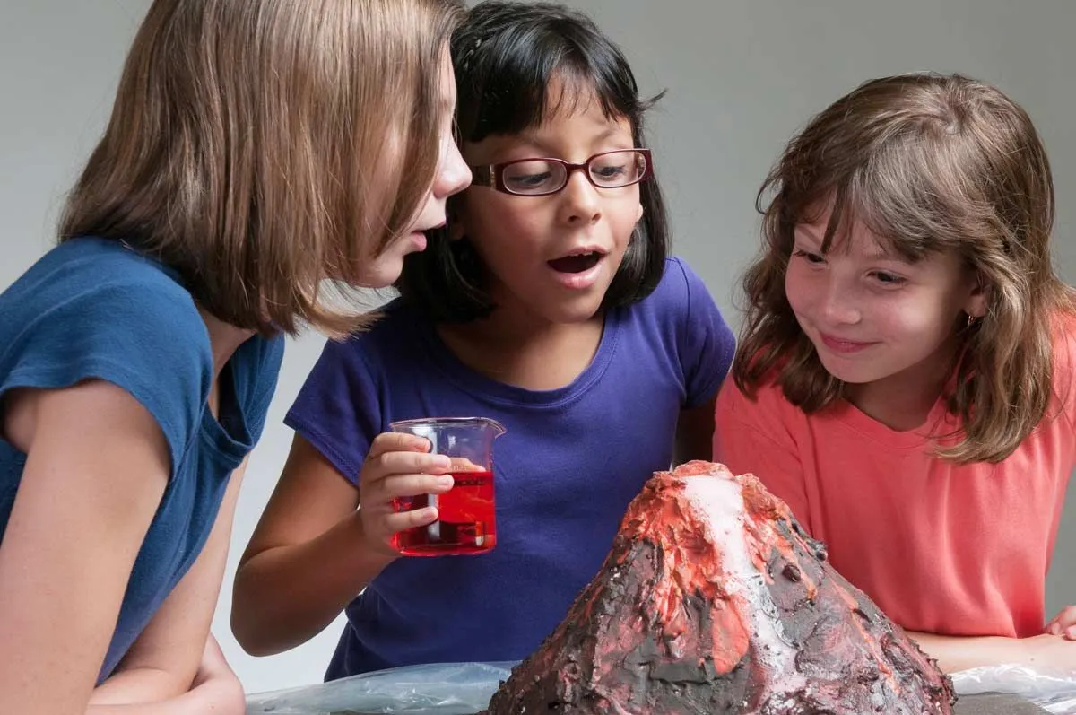 Three girls amazed at an experiment they are carrying out: making a model volcano eruption.