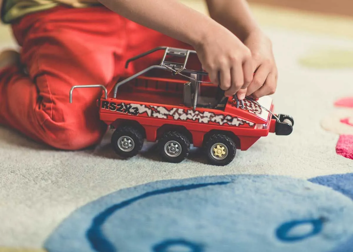 Close up of a child kneeling on the floor playing with their red toy truck.