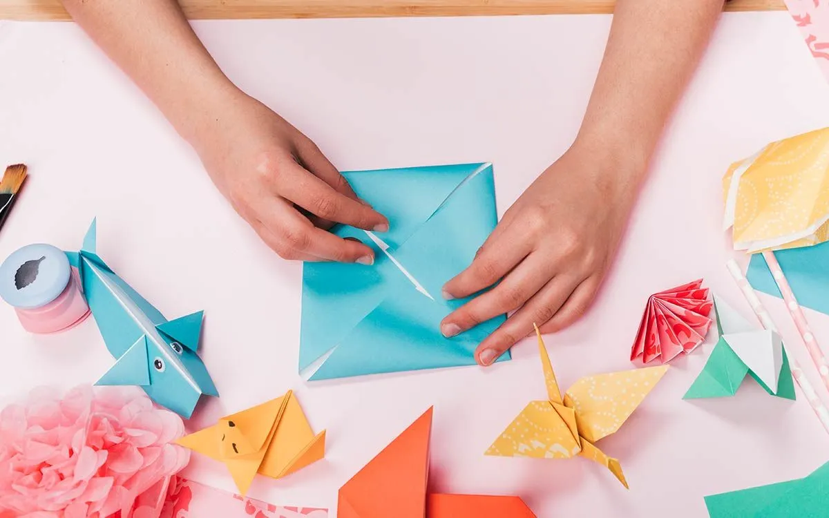 A child's hands folding a piece of origami paper to make an origami spider.
