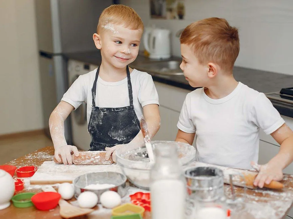 Two young boys smiling as they bake a Batman cake together.