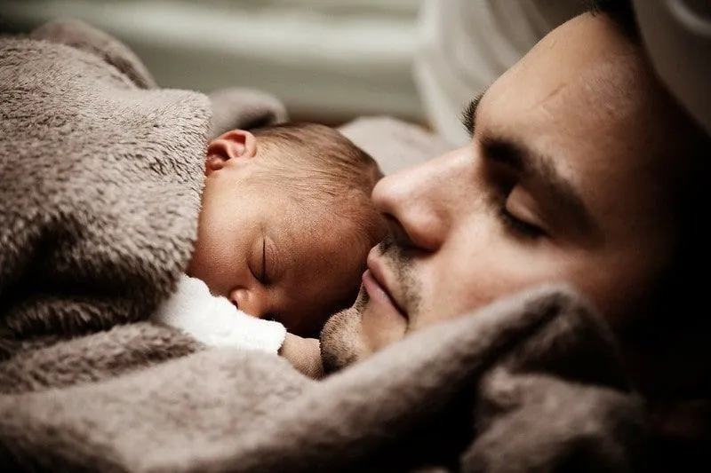 A newborn baby sleeping in a brown blanket on her father's chest