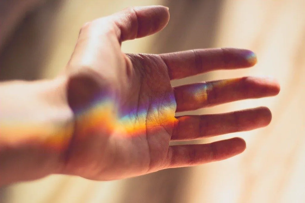A hand held out with a rainbow of refracted light on it.