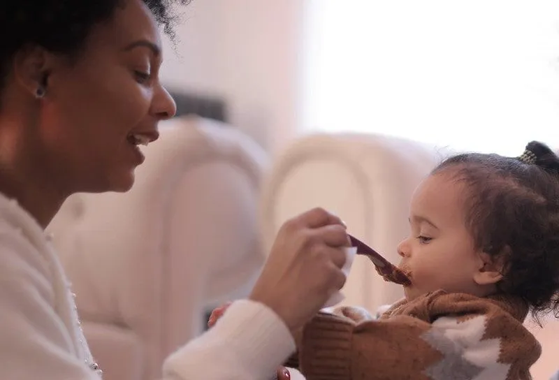 Mum feeds her little daughter with a spoon making noises to make her eat.