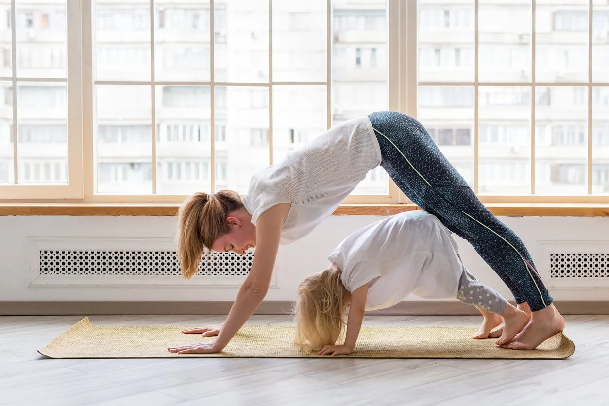 A mum and young daughter doing yoga together in a bright lit room with lots of windows. Image