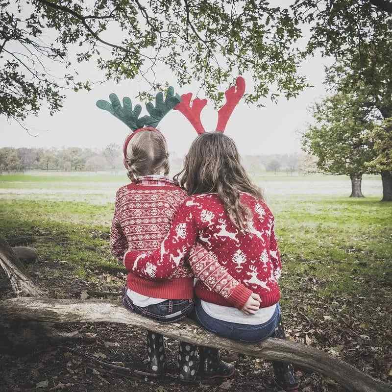 Sister's wearing Christmas jumpers sitting on a bench.