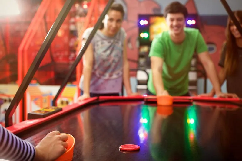 People surrounding air hockey table having fun. 