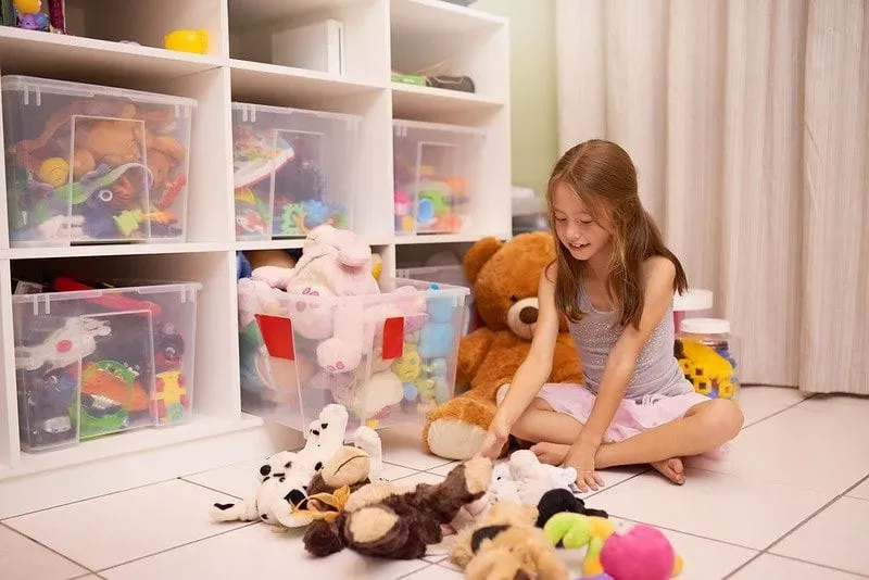 Child with cuddly toys spread out on floor. 