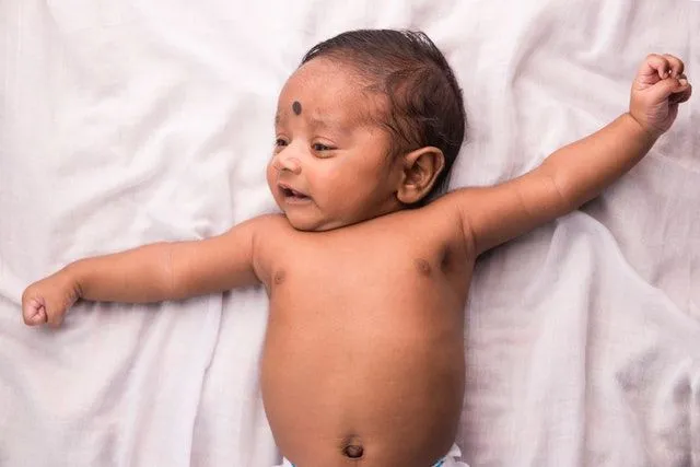 A newborn Pakistani boy stretching while lying on white sheets on bed - Baby names