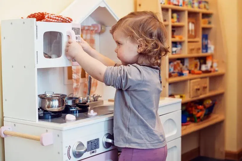 Girl having fun using toy washing machine in toy kitchen. 