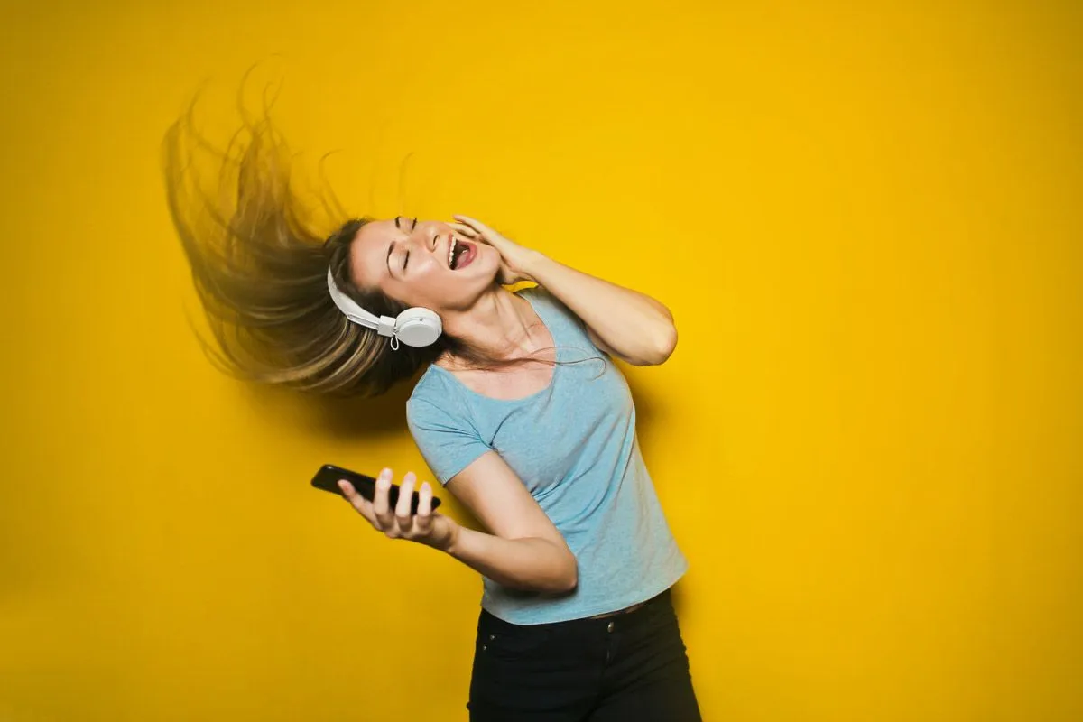 A woman listening to music wearing white headphones on yellow background
