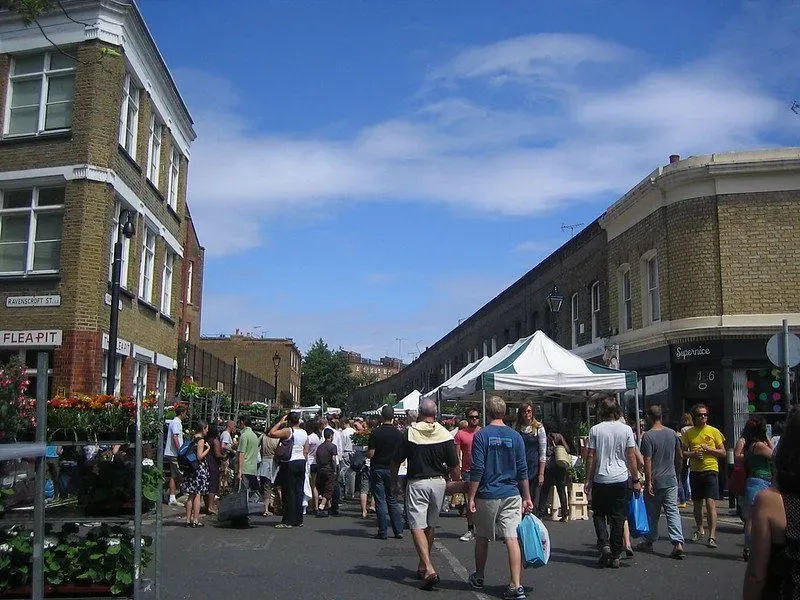 People walking towards the entrance of Columbia Road Flower Market with a blue sky.