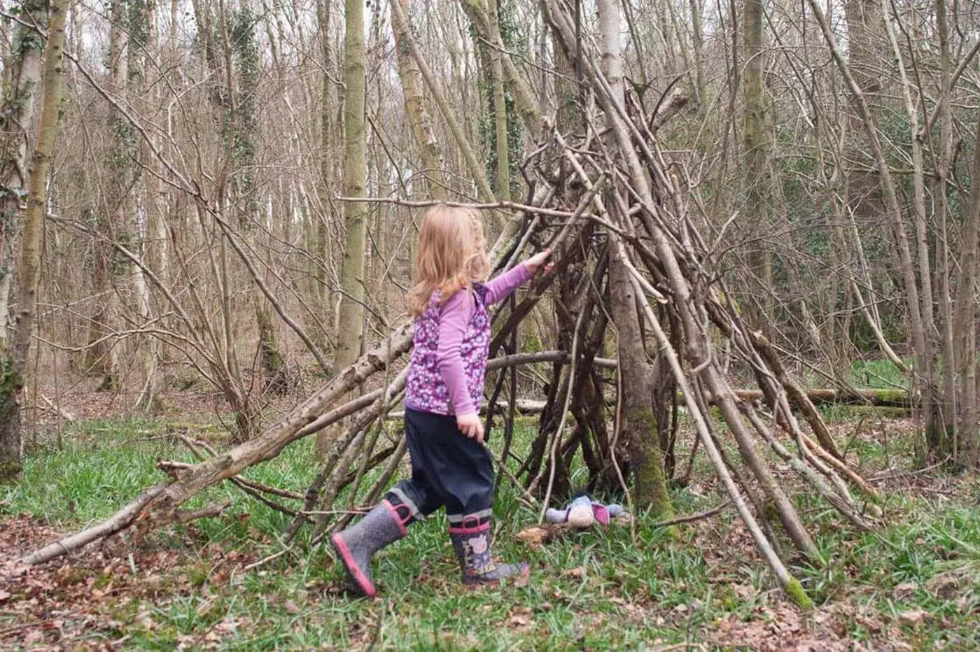 A young girl building a den out of sticks in woodland at Ashdown Forest.
