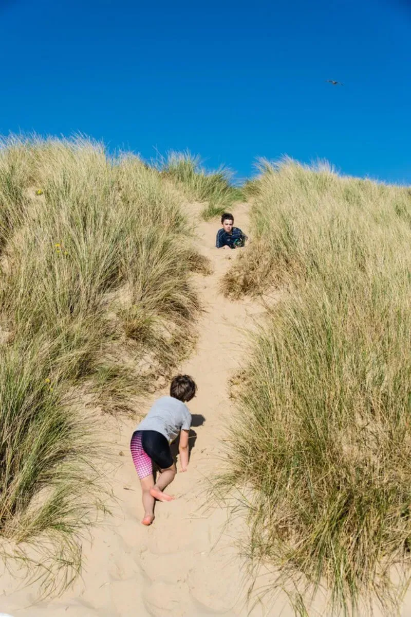 Children playing on the dunes at Camber Sands, with a blue sky in the background.