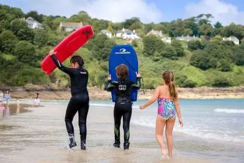Three kids walking along Carbis Bay Beach with their bodyboards.
