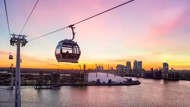 A cable car at Emirates Air Line against the London skyline, with a pink sunset.