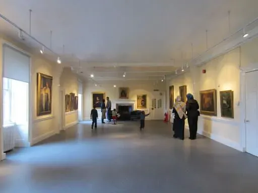 People looking at the paintings in the white exhibition space at Bruce Castle Museum.