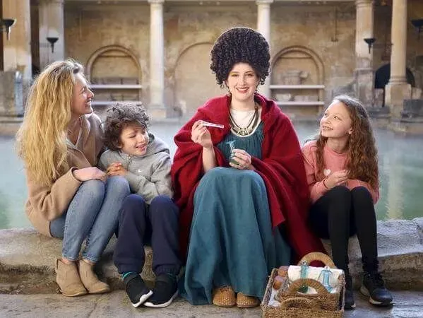 A family sitting next to one of the Roman Baths with a lady in Roman costume.