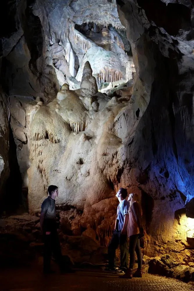 Two people on a tour of Cheddar Gorge Caves, with the stone lit up from beneath.
