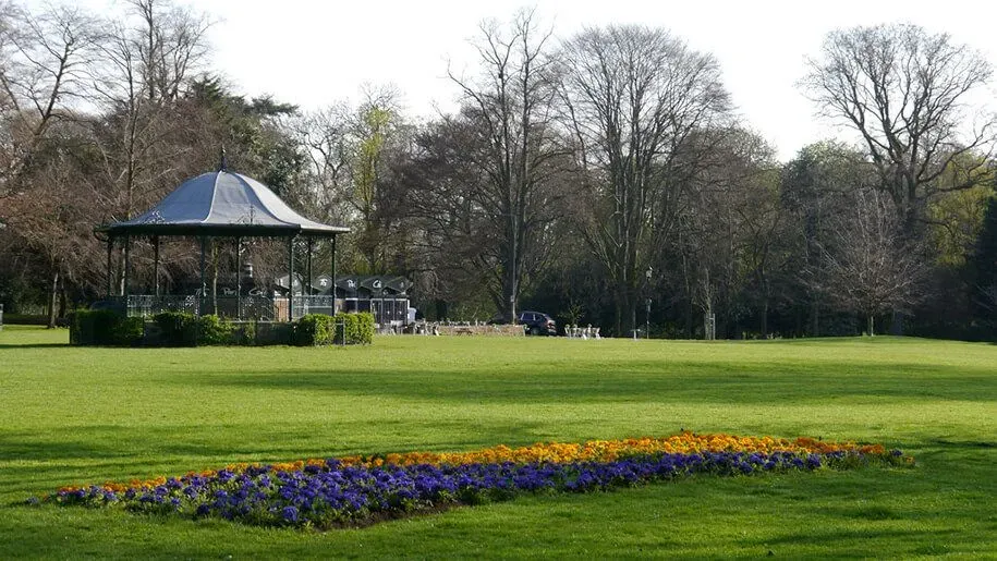 Bandstand in Abington Park with green grass and flowerbeds.