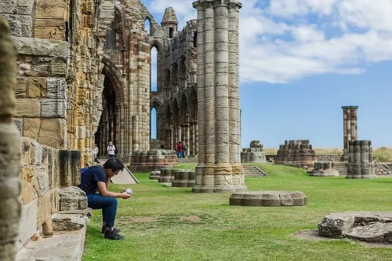 A man sitting and reading his guide at the ruins of Whitby Abbey.