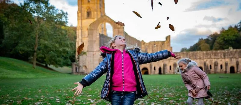 Two girls playing in Autumn leaves at Fountains Abbey and Studley Royal.