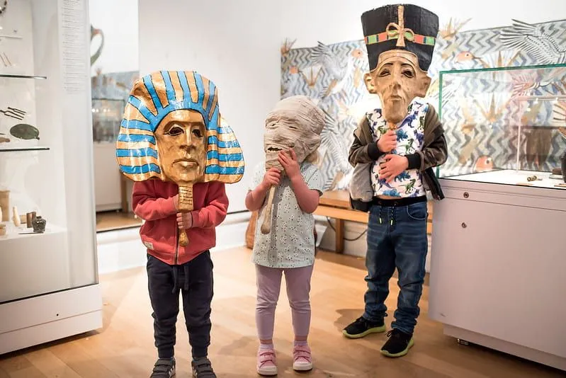 Three children wearing Egyptian masks at the Leicester Museum & Art Gallery.
