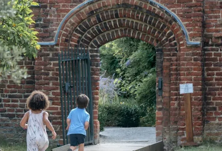Two kids running through stone doorway at Bishops Park.