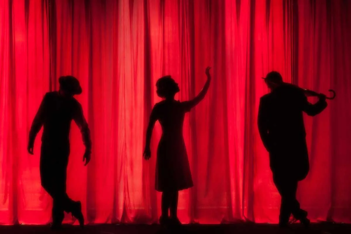 Silhouettes behind red theatre curtain.
