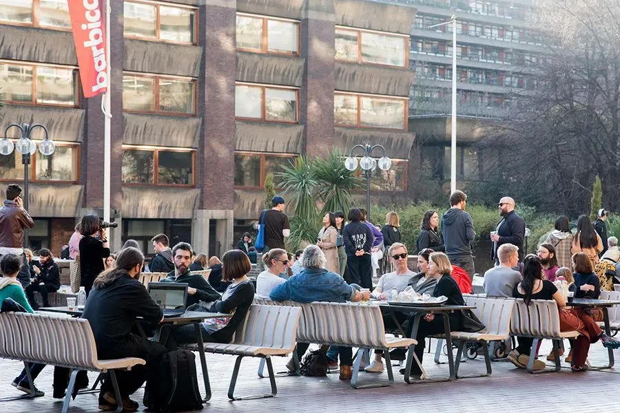 People socialising while sat at tables outside the Barbican Centre.