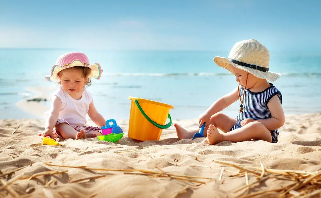 Two children play on beach with a bucket