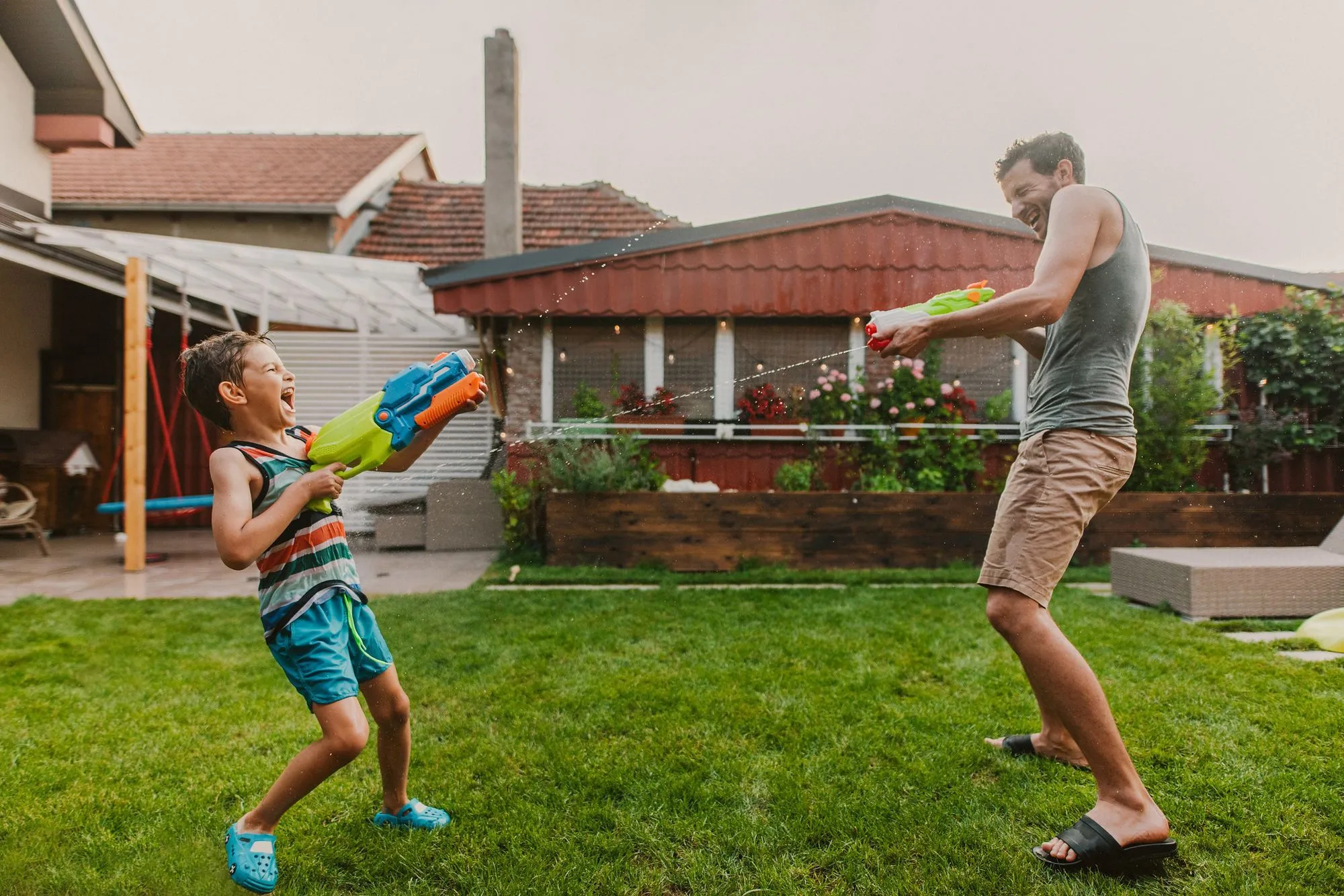 A boy and his father beat the heat with a water fight in garden. A good way to avoid heat stroke