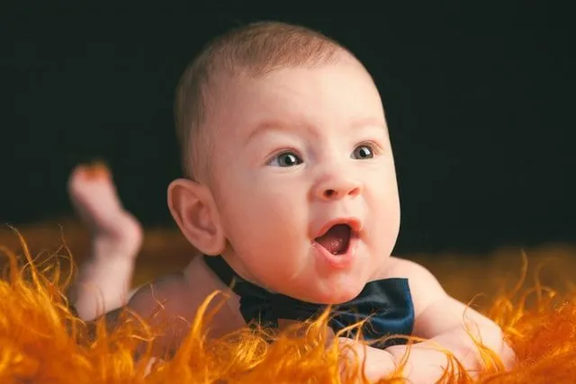 A newborn baby wearing black bow is lying on orange fur