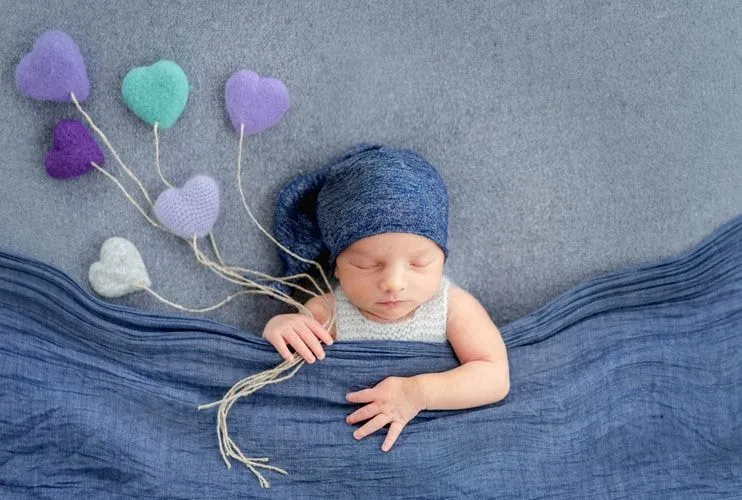A newborn baby sleeping under a blue blanket holding little blue hearts