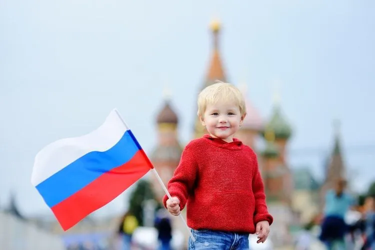 Cute toddler boy holding russian flag with Red Square and Vasilevsky descent on background