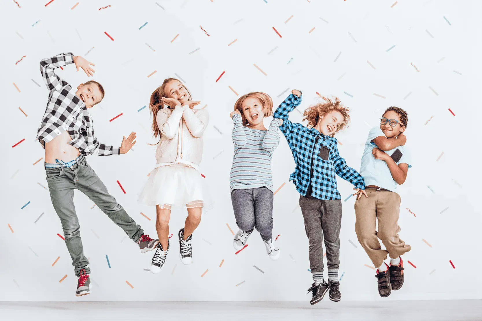 5 children jumping in joy against white background with confetti