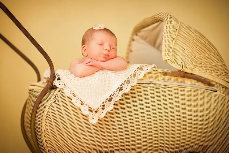 A newborn baby sleeping in a cradle wearing a tiny crown