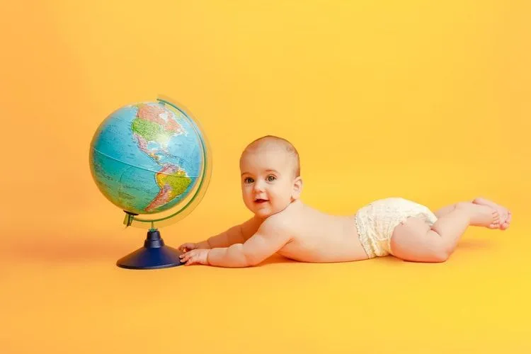 A newborn baby lying next to a globe on yellow background